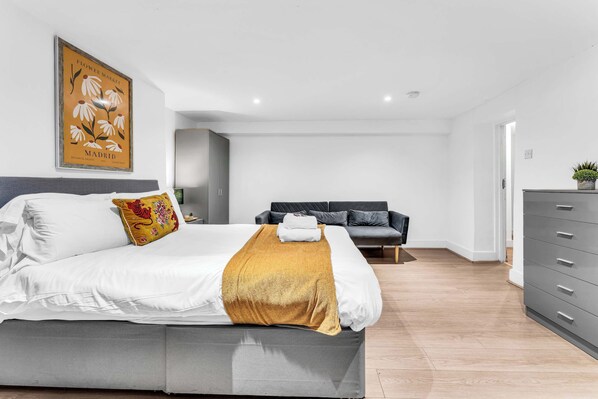 Un dormitorio moderno con cama, sofá, cómoda y una obra de arte colgada en la pared.