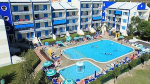Un hôtel à plusieurs étages doté d’une piscine centrale, d’un espace extérieur aménagé et d’une aire de jeux pour enfants.