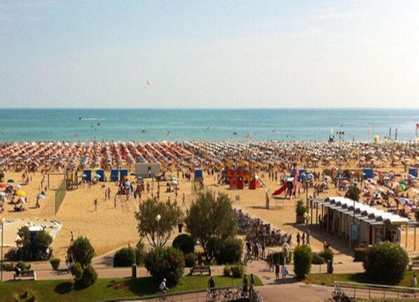 A beach with rows of umbrellas and beach chairs, a playground, and a few people.