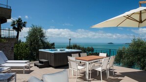 Eine Terrasse mit Whirlpool, Liegestühlen, einem Esstisch mit Stühlen und Blick auf das Meer.