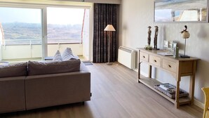 Ein modernes Wohnzimmer mit einer Couch, einem kleinen Tisch, einer Heizung und Blick ins Freie.