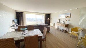 Ein modernes Hotelzimmer mit Essbereich, einer Couch, einem Fernseher und Blick ins Freie.