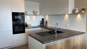 Eine moderne Küche mit weißen Schränken, einem eingebauten Backofen, einer Mikrowelle, einem Spülbecken mit modernem Wasserhahn und Holzregalen über der Arbeitsfläche.