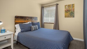 A bedroom with a bed, a nightstand, a lamp, a window with blinds, and a painting on the wall. - Beautiful 2BR APT 2 ⭑ Netflix & Keurig ⭑ Full Kitchen ⭑ WiFi ⭑ AC (Spokane Valley)