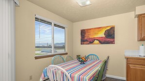 A dining area with a table covered in a striped tablecloth, surrounded by chairs, a window with blinds, and a painting on the wall. - Beautiful 2BR APT 2 ⭑ Netflix & Keurig ⭑ Full Kitchen ⭑ WiFi ⭑ AC (Spokane Valley)