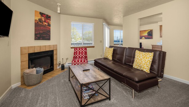 A living room with a fireplace, a brown leather sofa, a wooden coffee table, and a red patterned chair. - Beautiful 2BR APT 2 ⭑ Netflix & Keurig ⭑ Full Kitchen ⭑ WiFi ⭑ AC (Spokane Valley)