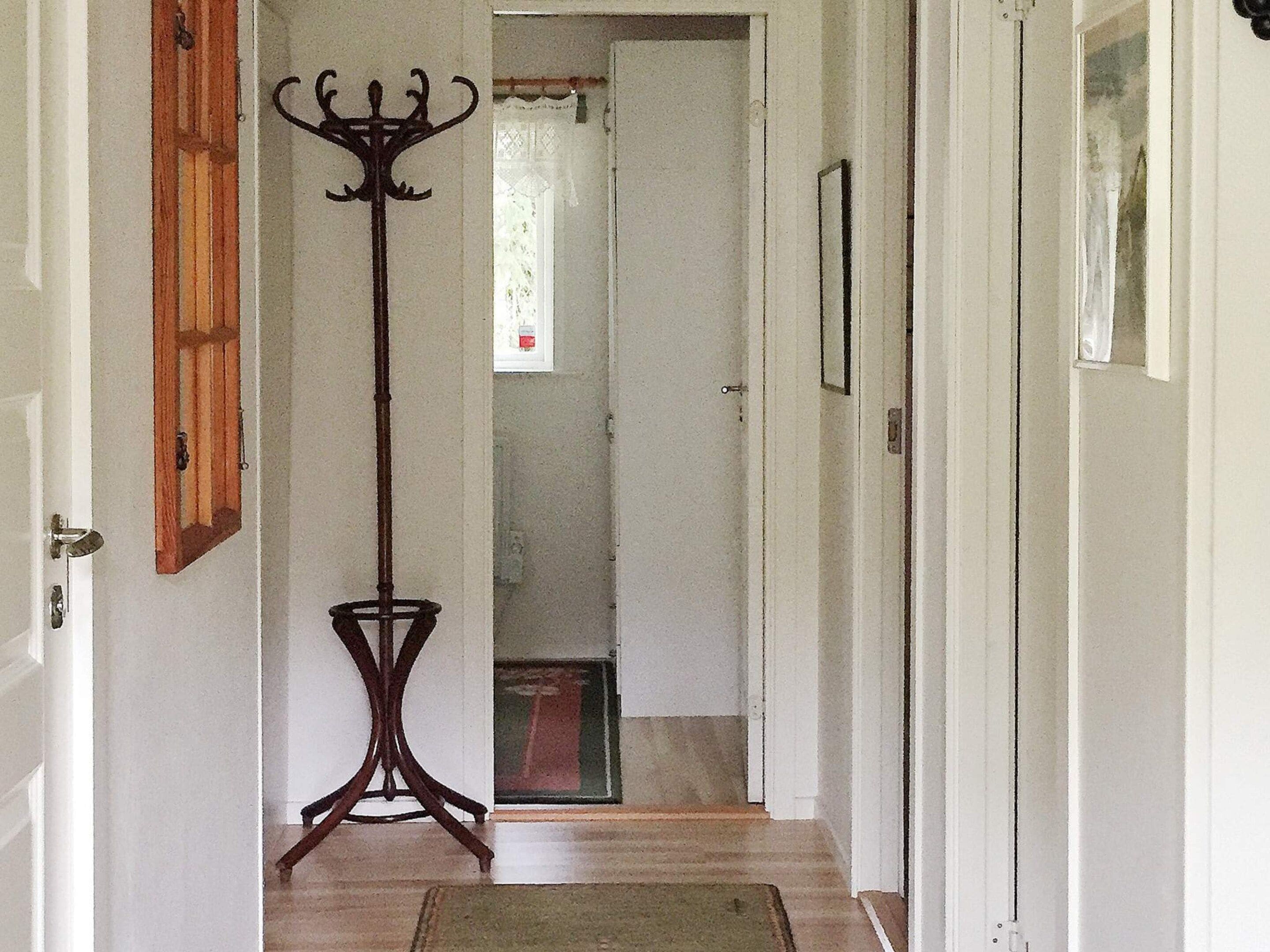 A hallway with a wooden floor, a coat rack, and a door leading to another room.