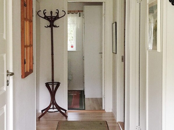 A hallway with a wooden floor, a coat rack, and a door leading to another room.