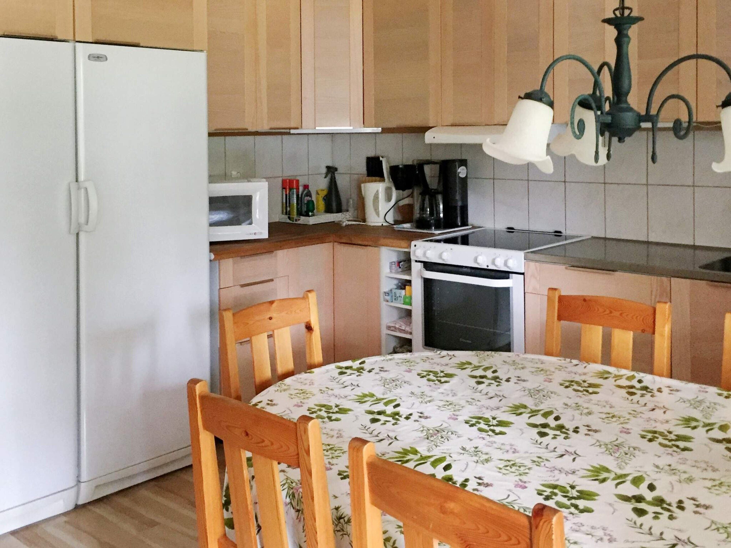 A compact kitchen with a refrigerator, microwave, stove, and a dining table with chairs.