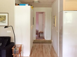 A narrow hallway with a wooden floor, leading to a room with a bed and a chair. A refrigerator is on the right side, and a lamp is on the left. - 4 Star Holiday Home in Gotlands Tofta (Gotlands Tofta)