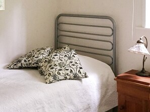Una cama con cabecera de metal, dos almohadas estampadas y una lámpara de noche sobre una mesita de madera.