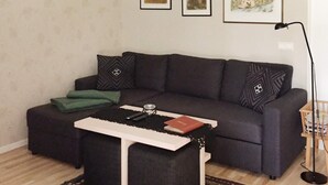 A living room with a dark grey sofa, a matching ottoman, a white coffee table, and a patterned rug. There are framed pictures on the wall and a floor lamp. - 4 Star Holiday Home in Gotlands Tofta (Gotlands Tofta)