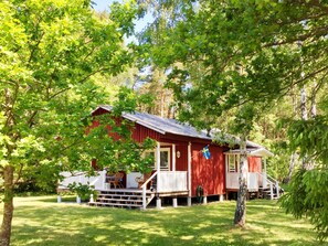 A red wooden cabin with a porch, surrounded by lush green trees. - 4 Star Holiday Home in Gotlands Tofta (Gotlands Tofta)