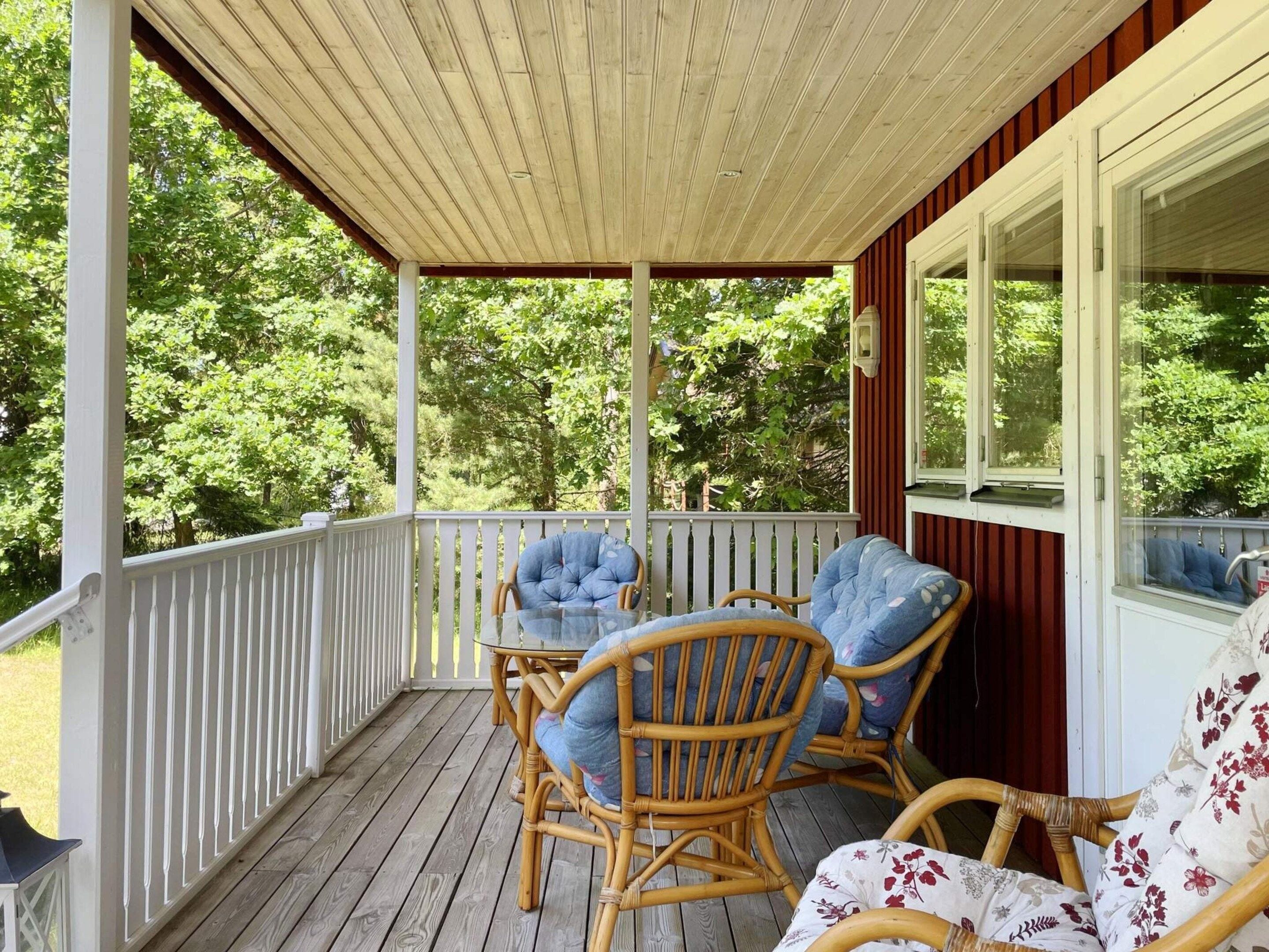 A covered porch with wicker furniture and a glass table.