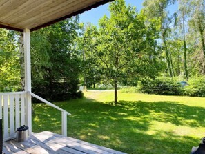 A wooden deck with a metal trash can, surrounded by lush greenery and trees.