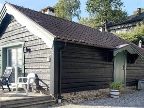A wooden cabin with a sloped roof, a porch with two chairs, and a potted plant. - 4 Star Holiday Home in Bastad (Bastad)