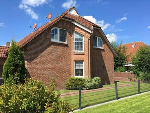 A two-story brick house with a sloped roof, satellite dish, and a fenced yard. - Holiday Home Heitmann (Dornum)