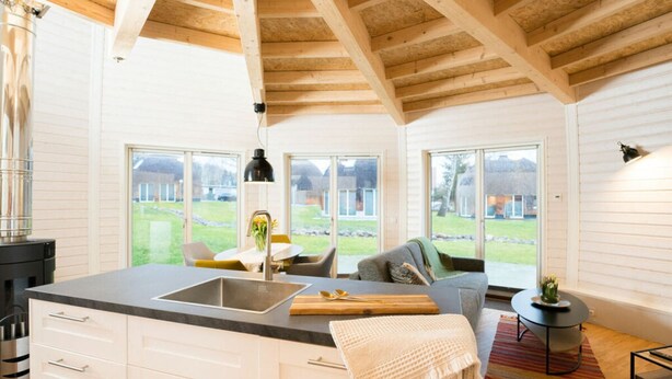 A modern kitchen with a large island, white cabinetry, and a view of the outdoors. - Kugelhaus Phoebe (Penzlin)