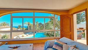 A room with a large arched window overlooking a pool and palm trees. - Villa La Seldeta by Solidays - Moraira, Costa Blanca (Moraira)