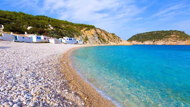 A pebble beach with clear blue water, white buildings with blue doors, and a green hillside in the background. - Villa La Seldeta by Solidays - Moraira, Costa Blanca (Moraira)