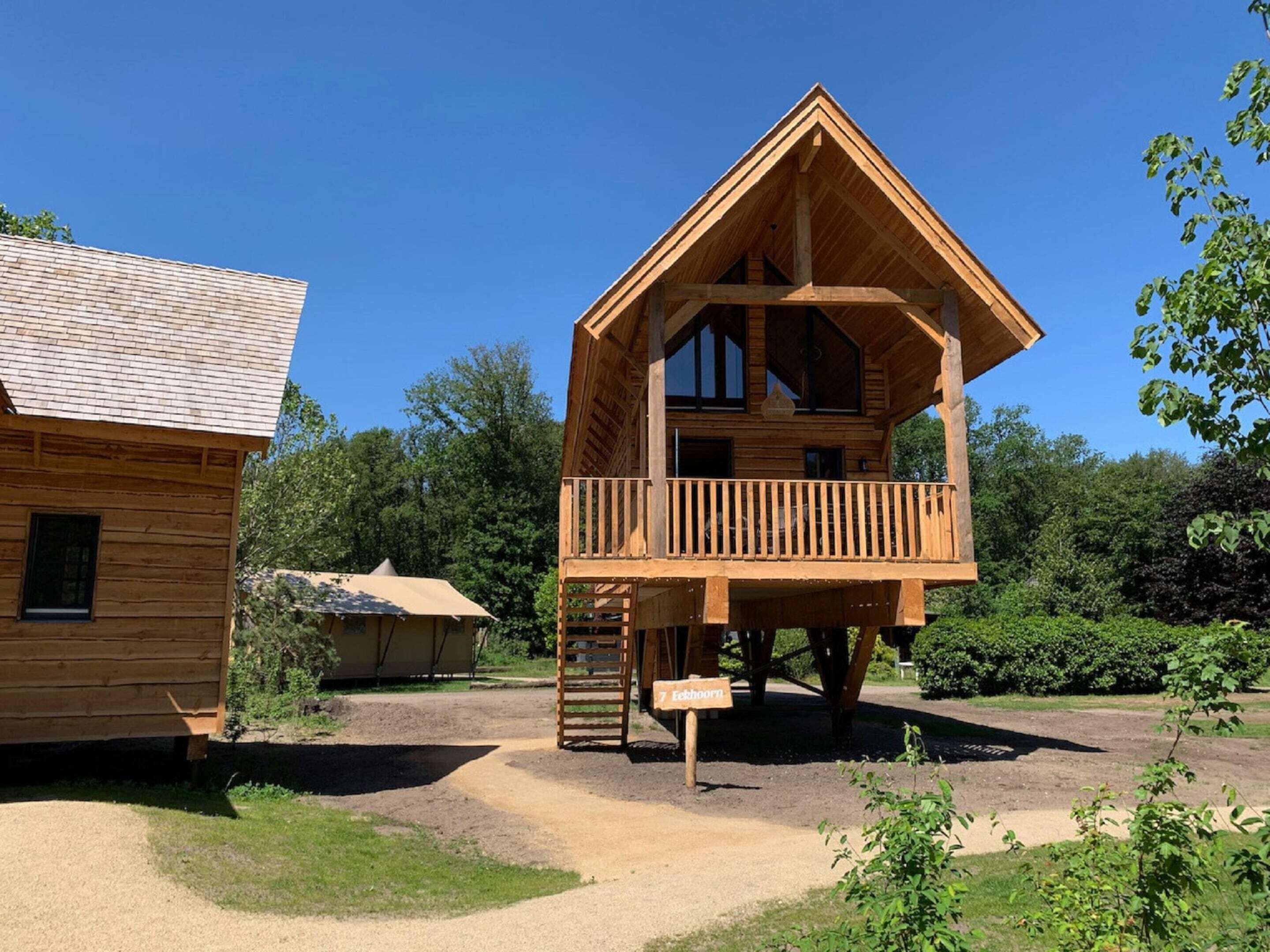 A wooden cabin with a balcony, a dirt path, and surrounding greenery.