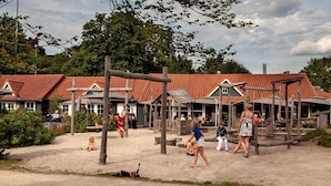 A sandy outdoor area with wooden play structures and a building with a red-tiled roof.