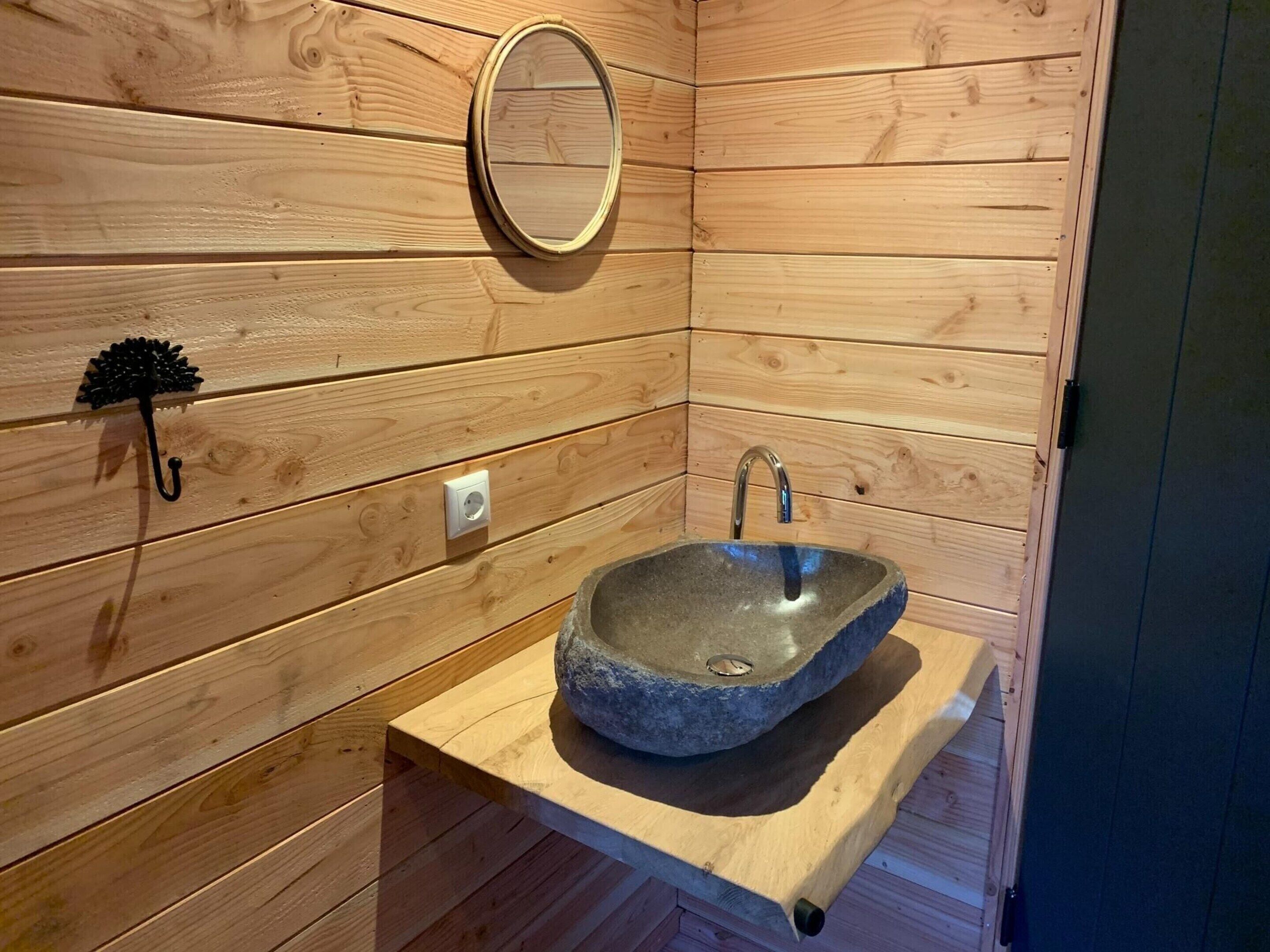 A wooden cabin interior with a stone sink, a mirror, and a wall-mounted light fixture.