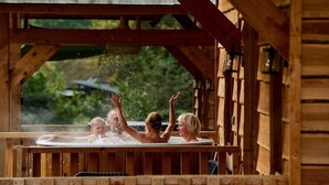 A wooden cabin with a hot tub where people are enjoying the water.