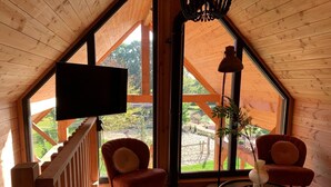 A cozy loft bedroom with a large window, wooden ceiling, and a flat-screen TV.