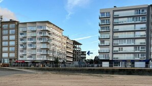 A multi-story building with balconies, a sandy foreground, and a clear sky. - Cozy Apartment With a top Location (Koksijde)