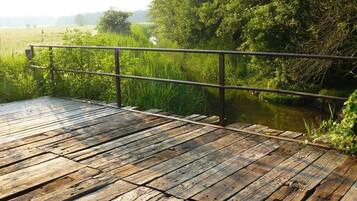 A wooden deck with a metal railing overlooking a river and greenery.