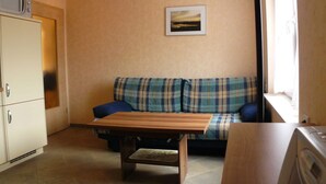Una sala de estar con un sofá a cuadros, una mesa de centro de madera, un microondas y una lavadora.