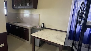 A compact kitchen with a sink, dark cabinets, a small table, and a curtain. - JVR Island in the Sky Resort (Balamban)