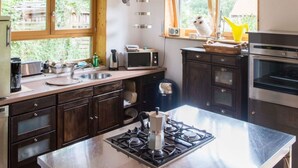 A modern kitchen with wooden cabinets, a gas stove, a microwave, and a large window with a view of greenery. - Huis aan het Park (Bispingen)