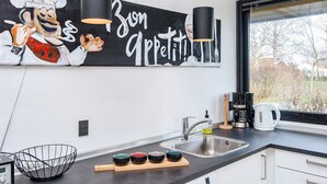 Moderni keittiö, jossa on Bosch-astianpesukone, musta työtaso, ikkuna, josta avautuu näkymä puita kohti, ja seinällä oleva kokin kuva.