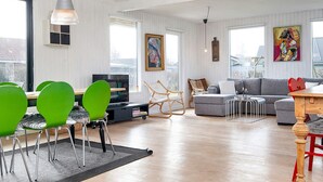 Moderni olohuone, jossa on puulattia, vihreät tuolit, harmaa sohva sekä ruokailutila, jossa on pöytä ja tuolit.