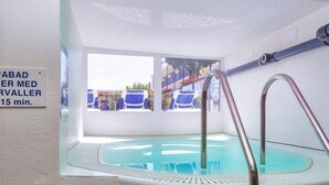 Una pequeña piscina interior con pared de vidrio, escalera metálica y un cartel que indica un tiempo de espera de 15 minutos.