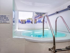 Una pequeña piscina interior con pared de vidrio, escalera metálica y un cartel que indica un tiempo de espera de 15 minutos.