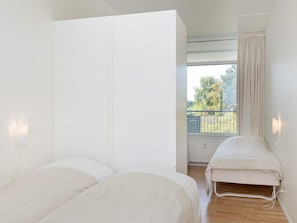 Quarto com duas camas, janela com vista para árvores e varanda com grades.