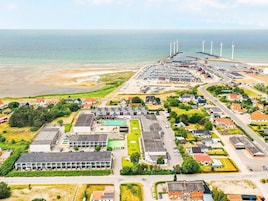 Vista aérea de un pueblo costero con un puerto deportivo, aerogeneradores y zonas residenciales.