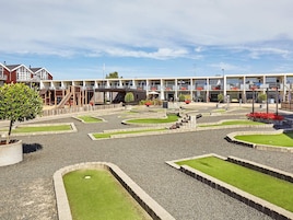Un patio con zona de juegos infantiles, un pequeño puente y un edificio con varios balcones y mesas al aire libre.