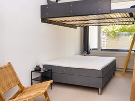 Un dormitorio pequeño con una cama litera, una mesita de noche, una silla y una ventana con vistas a zonas verdes.