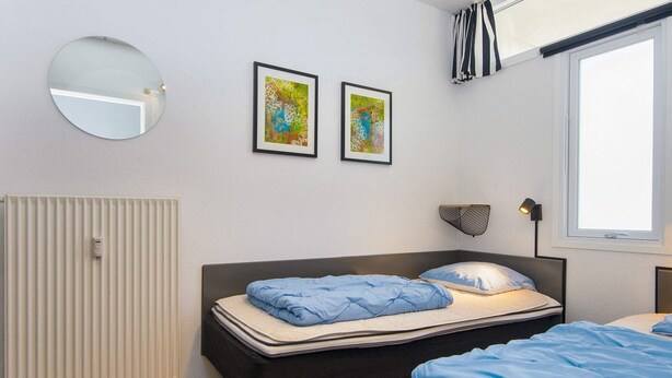 Un dormitorio con cama, radiador, ventana y dos cuadros en la pared.
