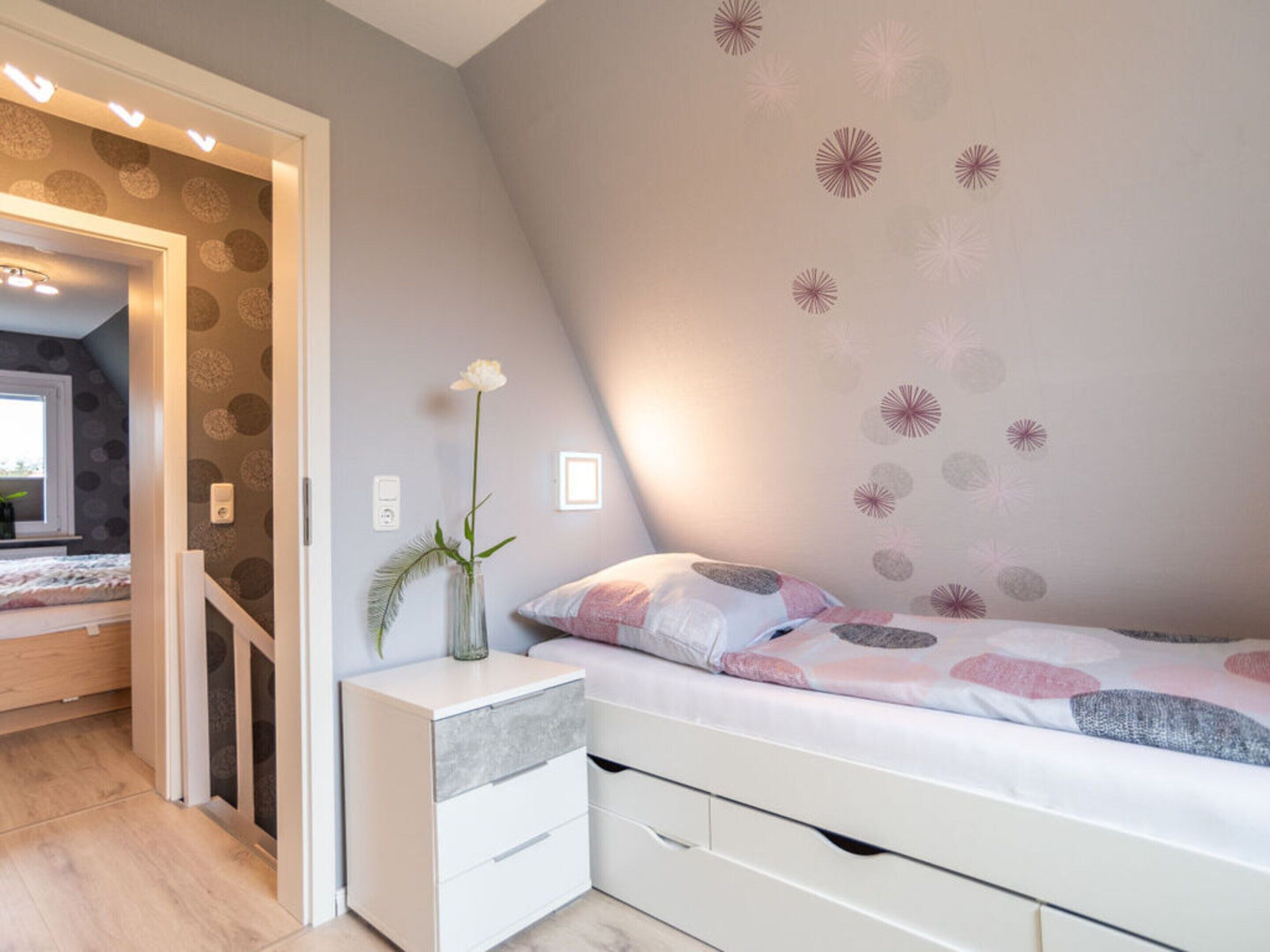 Ein Schlafzimmer mit einem Bett, einem Nachttisch, einer Vase mit einer Blume und einer Wand mit einem Rundmuster.