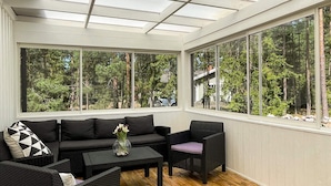 A sunroom with a wooden floor, black wicker furniture, and large windows offering a view of trees. - 4 Star Holiday Home in Monsteras (Monsteras)