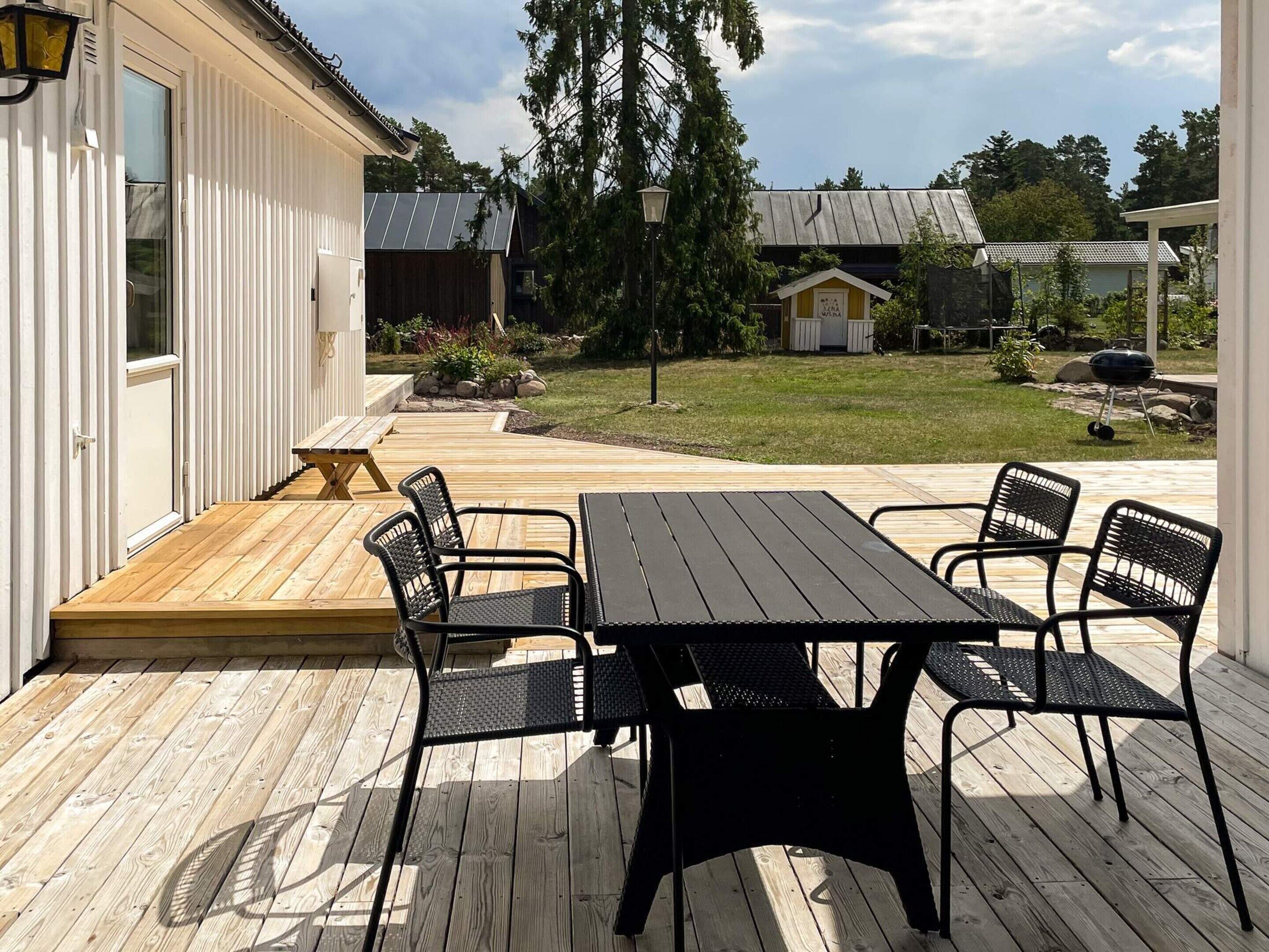 A wooden deck with a table and chairs, a small garden, and a building with a white exterior.