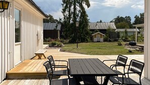 A wooden deck with a table and chairs, a small garden, and a building with a white exterior. - 4 Star Holiday Home in Monsteras (Monsteras)
