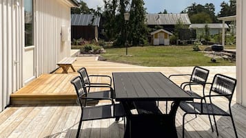 A wooden deck with a table and chairs, a small garden, and a building with a white exterior.