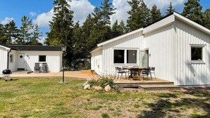 A white cabin with a deck and a dining area, surrounded by trees. - 4 Star Holiday Home in Monsteras (Monsteras)