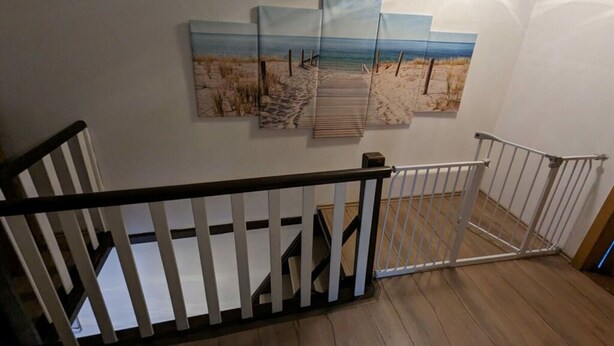 A staircase with a white railing, wooden steps, and a wall with three beach-themed paintings. - Huus Meta Modern Retreat (Krummhoern)